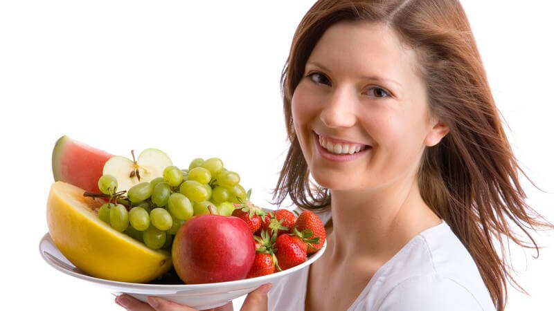Junge Frau trägt Teller mit frischem Obst, lacht in Kamera