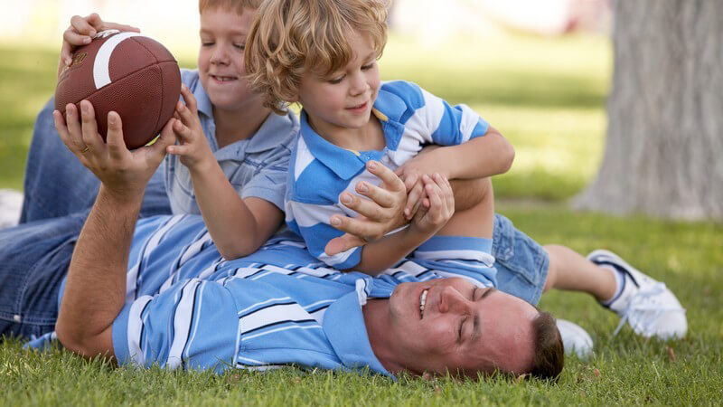Vater spielt mit Kindern Football auf Wiese