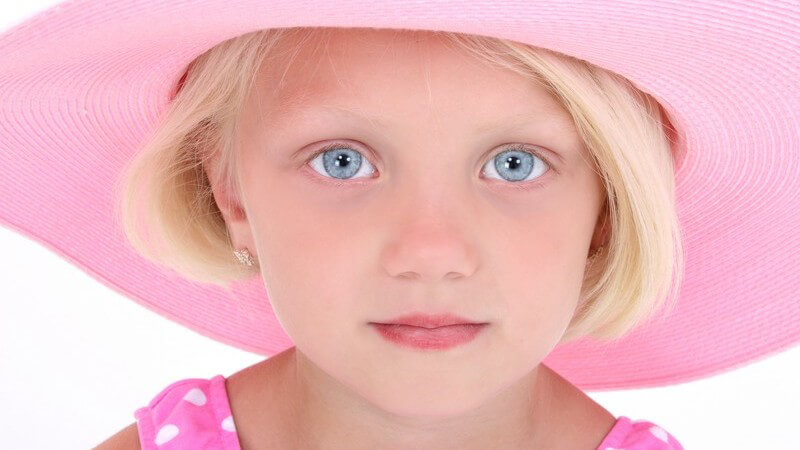 Kleines blondes Mädchen mit hellblauen Augen in rosa Badeanzug mit rosa Hut schaut in Kamera