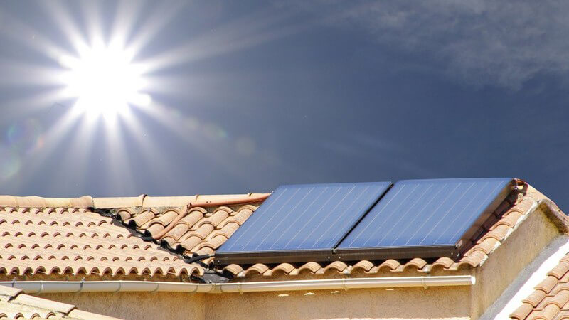 Dach mit Solarzellen, darüber strahlt die Sonne
