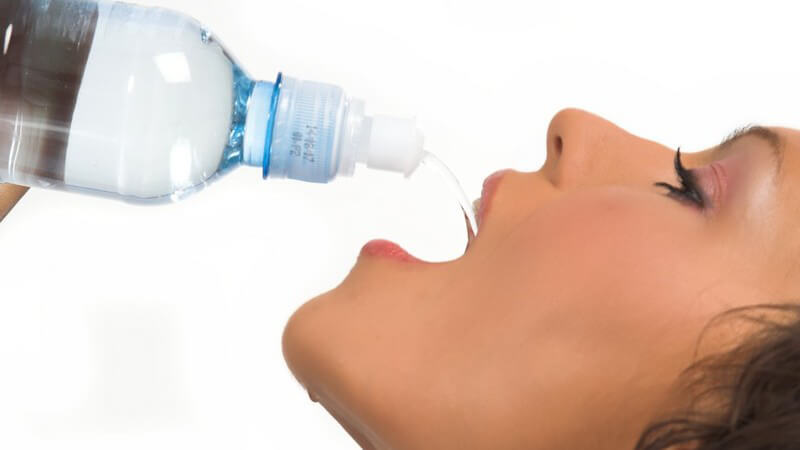 Dunkelhaarige Frau mit offenem Mund trinkt aus Wasser Plastikflasche