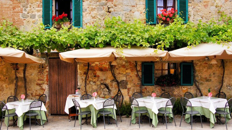 Bistro oder Café in der Toskana, gedeckte Tische unter Sonnenschirmen vor einem Haus