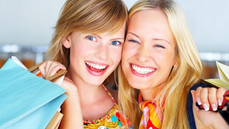 Zwei Freundinnen mit Einkaufstaschen nach Shopping, lachen in die Kamera