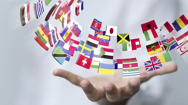 Internationale Geschäfte - geöffnete Hand eines Geschäftsmannes, darüber Symbole von Flaggen vieler Länder