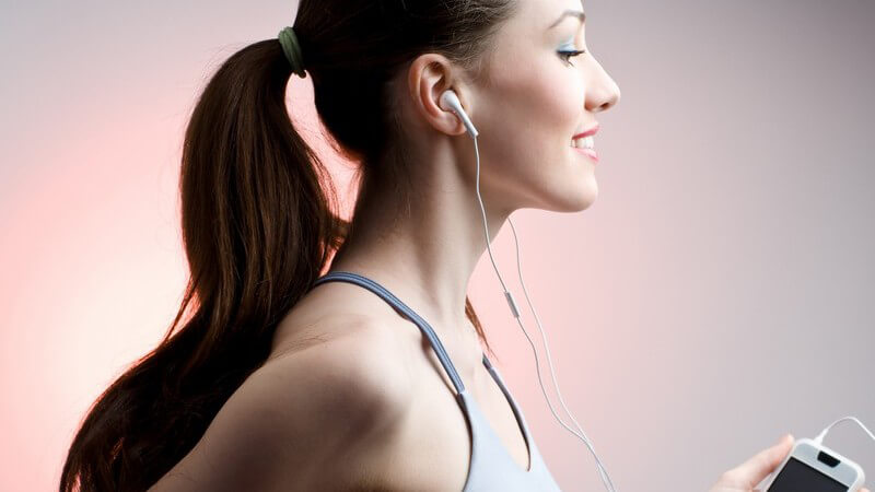 Junge Frau im Sportoutfit auf Laufband hört Musik über Kopfhörer