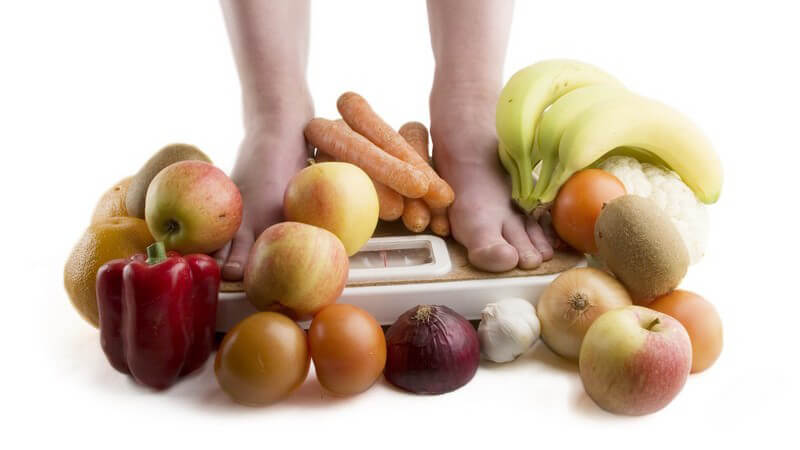 Abnehmen - Füße auf der Waage, umgeben von Obst und Gemüse