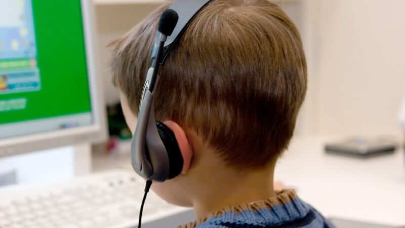 Kleiner Junge mit Headset sitzt vor dem Computer
