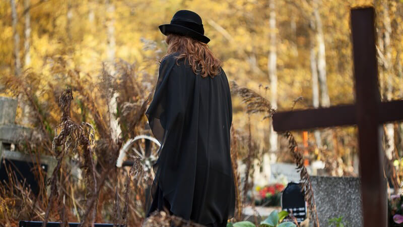 Schwarz gekleidete Frau, Witwe in Trauer besucht ein Grab auf dem Friedhof