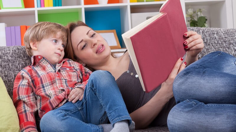 Vorlesen: Mutter mit Sohn auf der Couch, sie liest ihm etwas vor