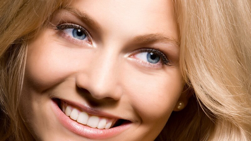 Gesichtsportrait einer jungen blonden Frau, sie lächelt an Kamera vorbei