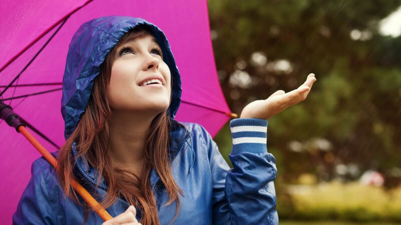 Frau in Regenjacke steht unter dem Regenschirm und prüft mit der Hand, ob es noch regnet