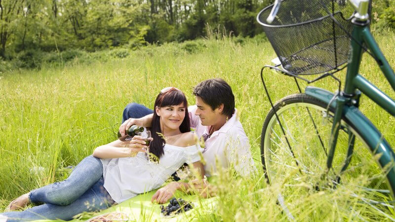 Junges Paar auf Wiese beim Picknick, im Vordergrund Fahrrad mit Korb