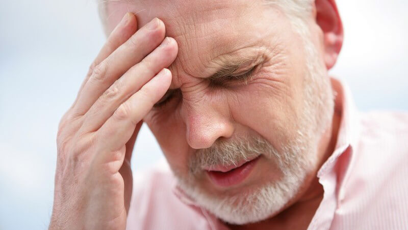 Älterer Mann fasst sich mit schmerzverzerrtem Gesicht an den Kopf