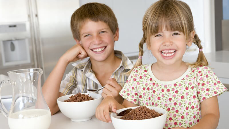 Zwei kleine Kinder am Frühstückstisch mit Müsli, beide lachen