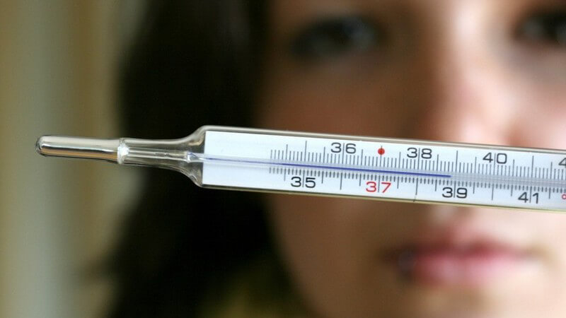 Krank - Frau hält Fieberthermometer vor das Gesicht