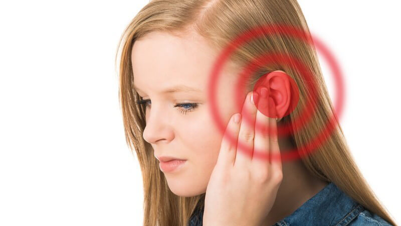 Junge Frau hält sich das Ohr, rot markiert, Tinnitus