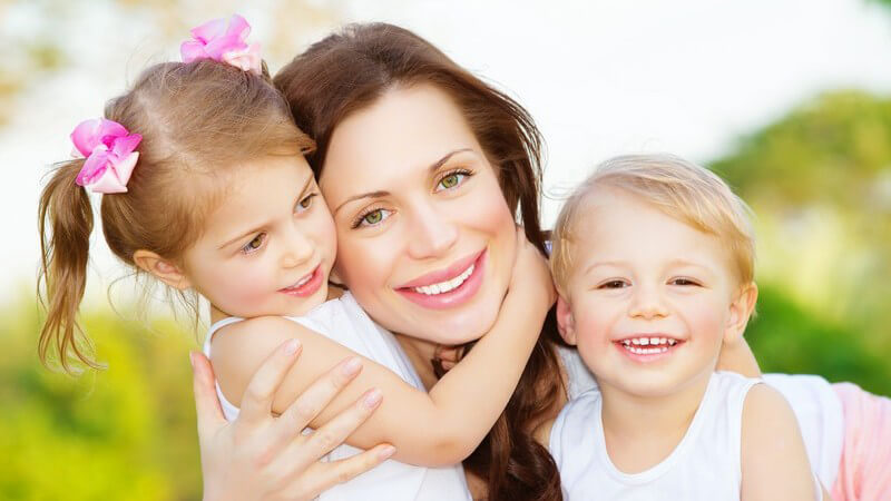 Junge Mutter mit Kindern, Zwillingen im Arm, draußen, alle drei lachen