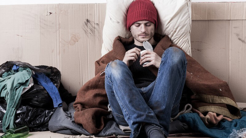Junger Obdachloser sitzt auf dem Boden und isst aus einer Konservendose