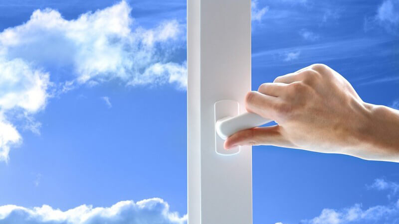 Rechte Hand an Fenstergriff, im Hintergrund strahlend blauer Himmel