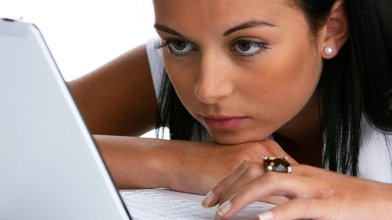 Junge, schwarzhaarige Frau hängt nah und konzentriert vor ihrem weißen Laptop