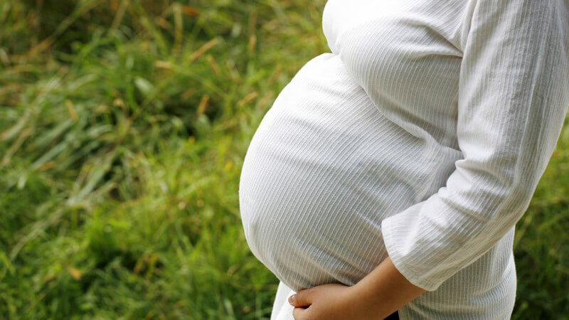 Seitenansicht Oberkörper einer schwangeren Frau in weißer Kleidung