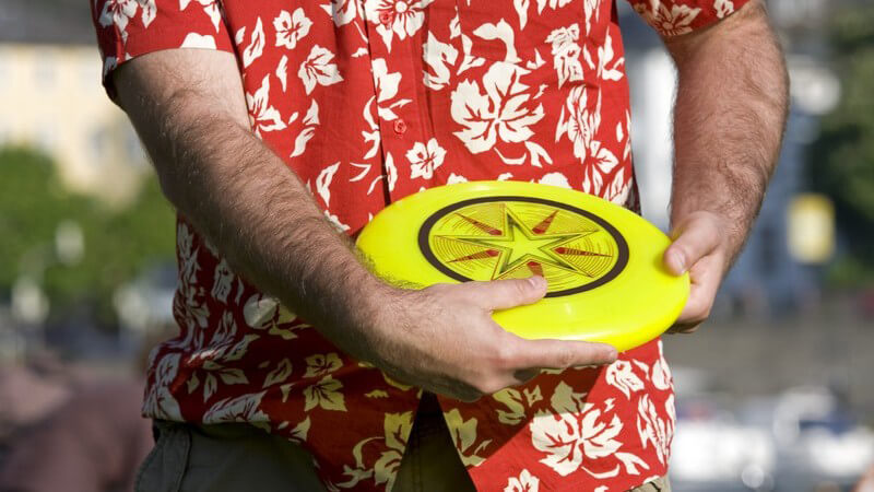 Mann im rot-weißen Hawaii-Hemd ist im Begriff, ein gelbes Frisbee zu werfen