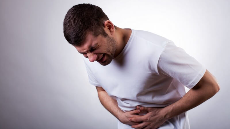 Bauchschmerzen, Magenschmerzen - Mann mit schmerzverzerrtem Gesicht krümmt sich, hält sich am Bauch