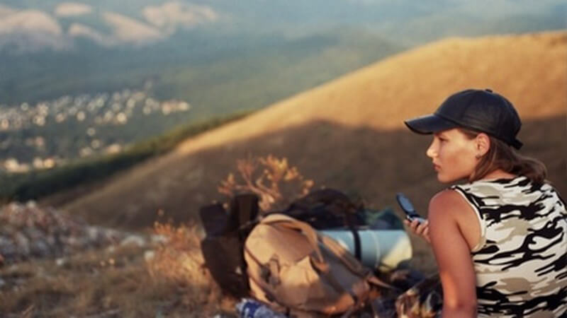 Junge Frau mit Kappe sitzt mit Wanderrucksack in einsamer Berglandschaft