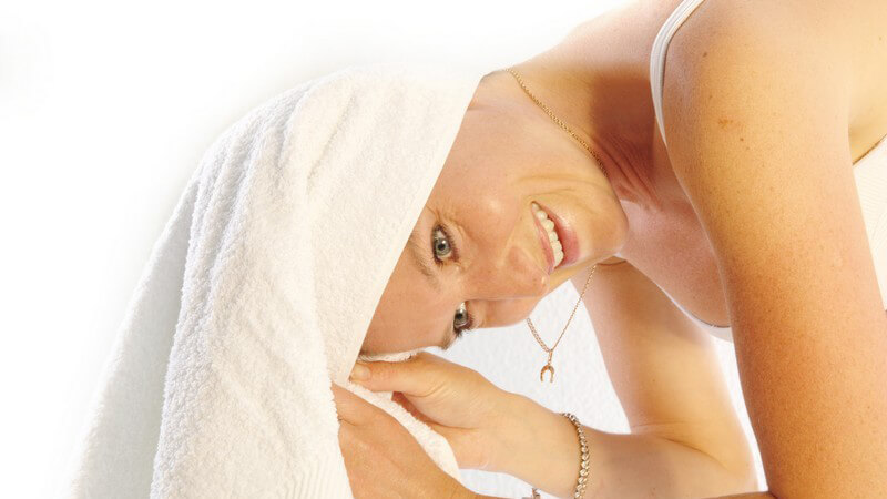 Lächelnde Frau steht vorn übergebeugt und wickelt sich Handtuch auf Kopf