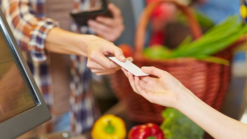 Bezahlen an der Supermarkt-Kasse: Frau reicht Kassiererin eine Kundenkarte oder eine Geldkarte