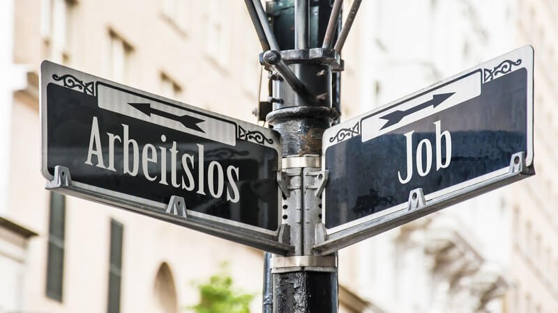 Zwei Straßenschilder oder Wegweiser zeigen mit einem Pfeil nach links ("Arbeitslos") bzw. rechts ("Job")