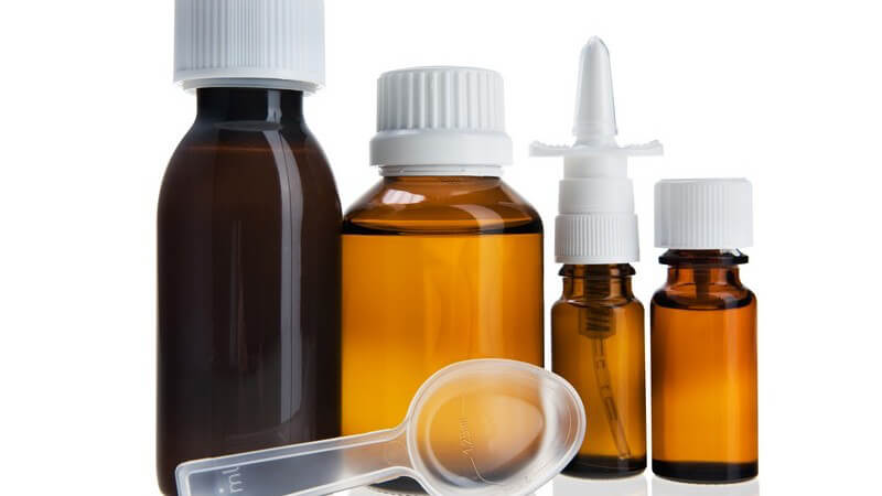 Arzneimittel - Transparenter Dosierlöffel liegt vor vier verschiedenen Medikamenten