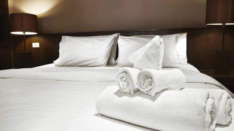 Doppelbett im Doppezimmer eines Hotels, darauf zusammengerollte Handtücher