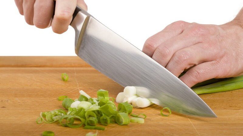 Frühlingszwiebeln werden mit Messer auf Brett geschnitten
