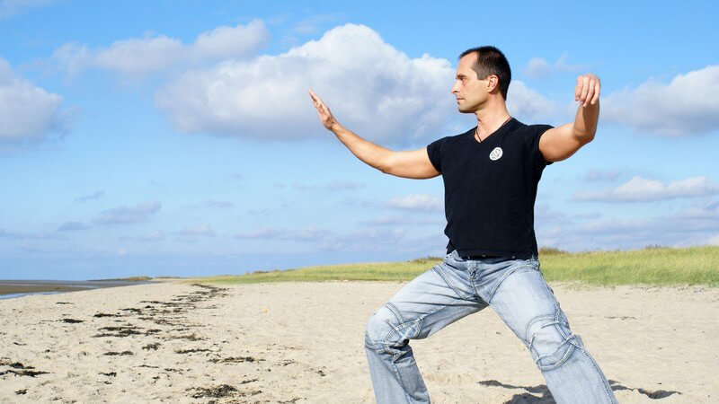 Mann macht Tai-Chi Übung am Strand unter blauem Himmel