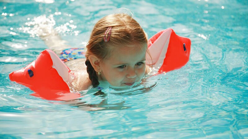 Kleines Mädchen mit Schwimmflügeln im Wasser