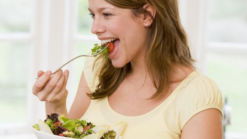 Schwangere, lächelnde Frau isst frischen Salat