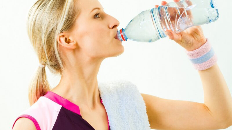 Junge, blonde Frau im Sportoutfit trinkt Wasser aus Flasche