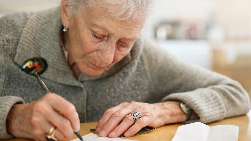 Alte Frau sitzt am Schreibtisch und schreibt