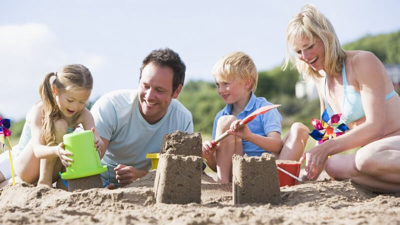 Paar mit zwei Kindern, Familie sitzt am Strand und baut Sandburgen