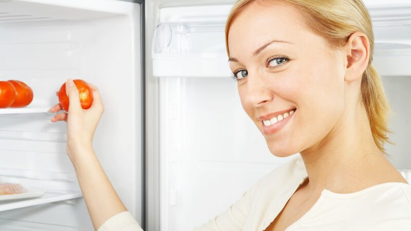 Blonde Frau am Kühlschrank holt Tomaten raus