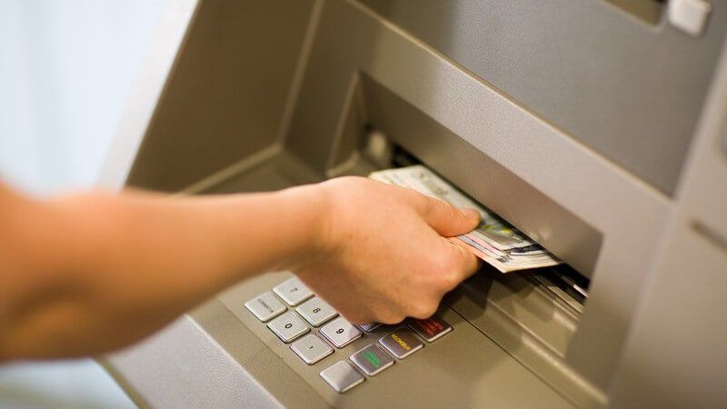 Rechte Hand zieht Geld aus Geldautomat heraus