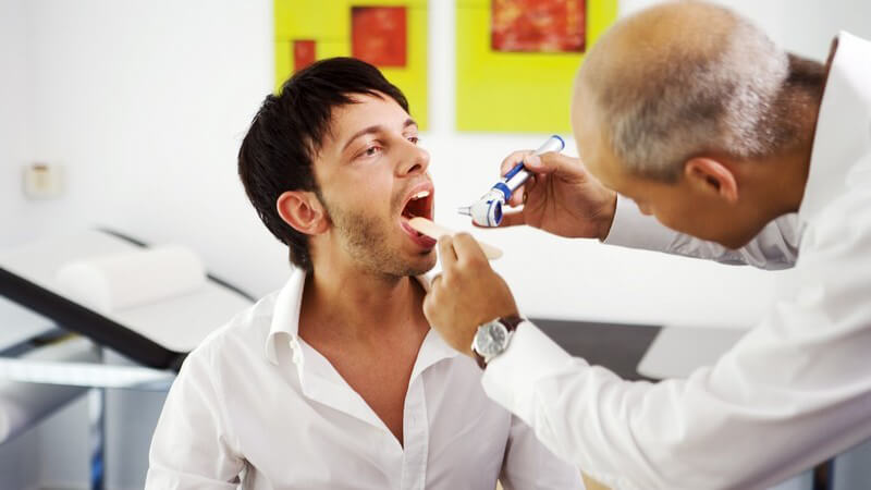 Arzt guckt jungem Mann in den Mund