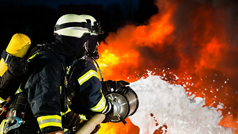 Feuerwehrmann löscht Feuer, Brand mit Schlauch