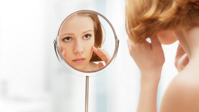 Gesicht einer jungen Frau im Kosmetikspiegel, sie sieht sich ihre Haut an