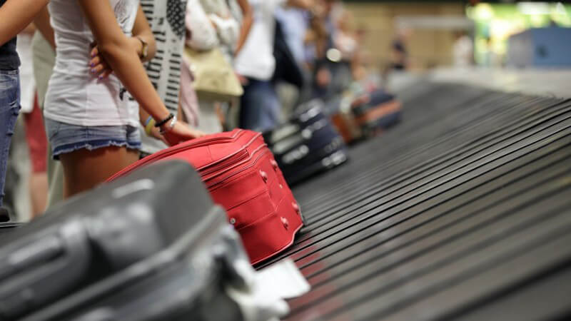 Gepäckausgabeband am Flughafen: Fluggäste warten an der Gepäckförderanlage auf ihre Koffer