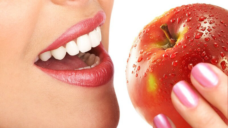 Frau mit Lippenstift und rosa Nagellack isst einen roten Apfel