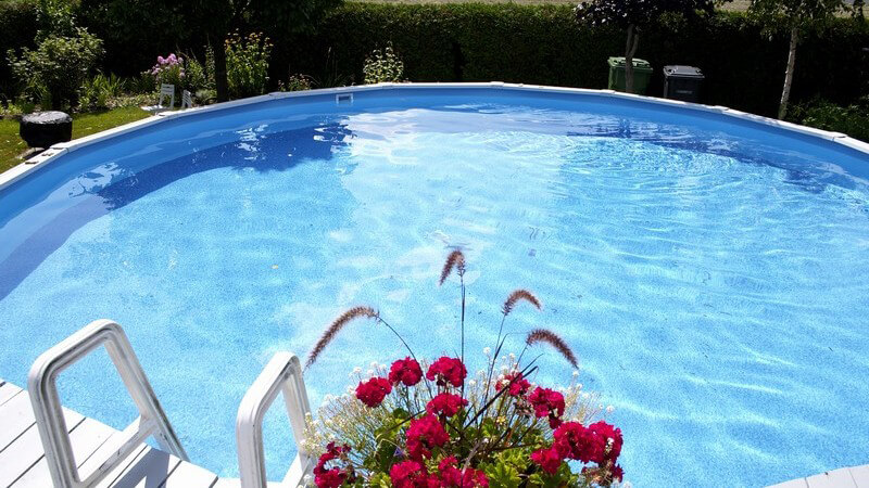 Runder Swimming Pool im Garten, am Rand rote Blumen