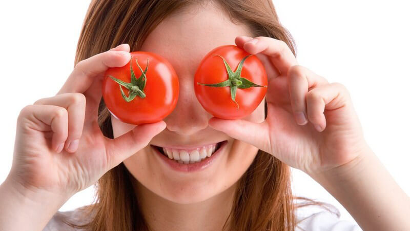Junge Frau, lächelnd, hält zwei frische Tomaten vor ihre Augen