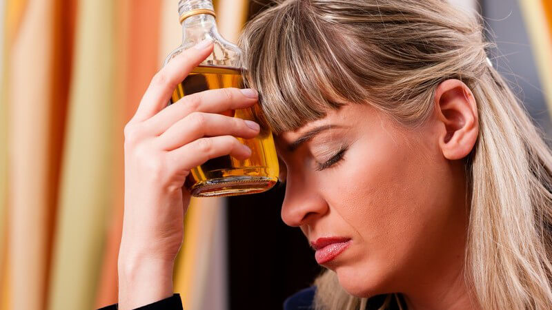 Alkoholmissbrauch: frustrierte Frau hält sich Flasche mit Alkohol an den Kopf
